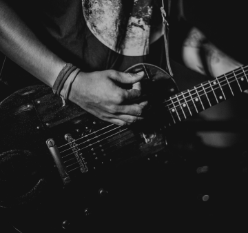 Braços de um homem segurando e tocando uma guitarra