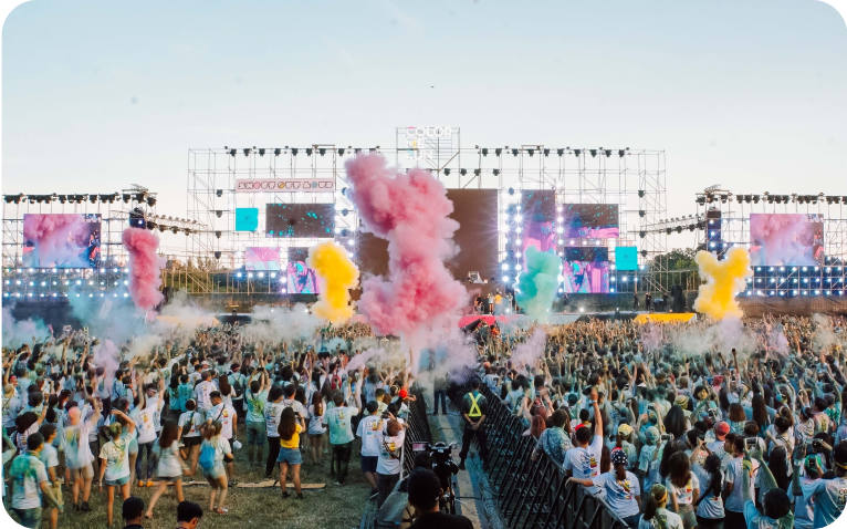 multidão voltada para o palco próximo e algums pontos na multidão com fumaça colorida